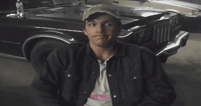 a man with a smiley face on his face is sitting in front of a car