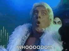 A Man With A Surprised Look On His Face Is Wearing A White Fur Coat And A White Feather Boa . GIF