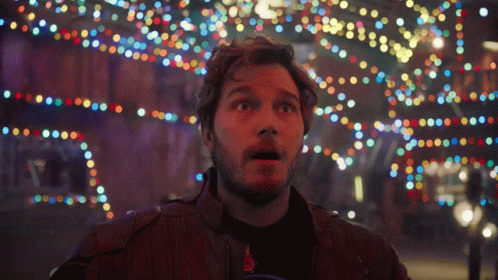 A Man With A Surprised Look On His Face Stands In Front Of A Bunch Of Colorful Lights GIF