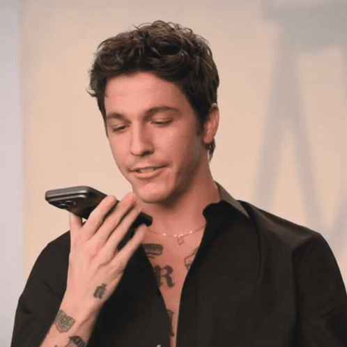 a man with a tattoo of the letter r on his chest holds a cell phone
