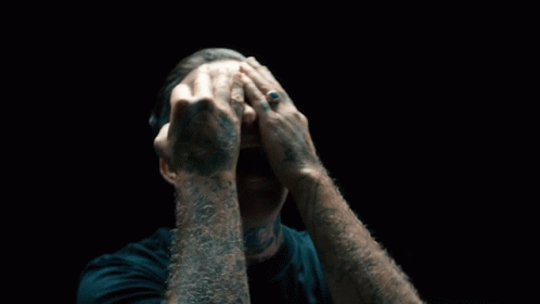 A Man With A Tattoo On His Arm Covering His Face GIF