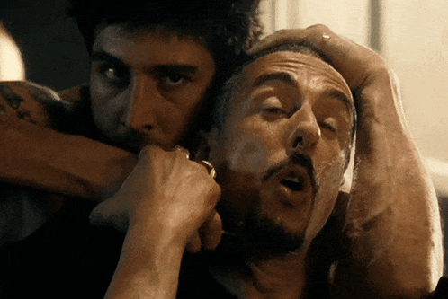 A Man With A Tattoo On His Arm Holds Another Man 'S Head In His Hands GIF