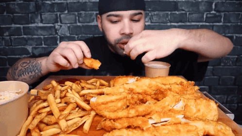 A Man With A Tattoo On His Arm Is Eating Fish And Fries GIF