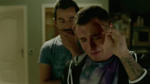 A Man With A Tattoo On His Arm Is Holding His Head While Another Man Holds His Hand To His Face . GIF
