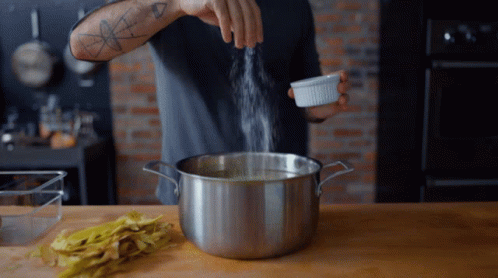 A Man With A Tattoo On His Arm Is Pouring Salt Into A Pot Of Water GIF