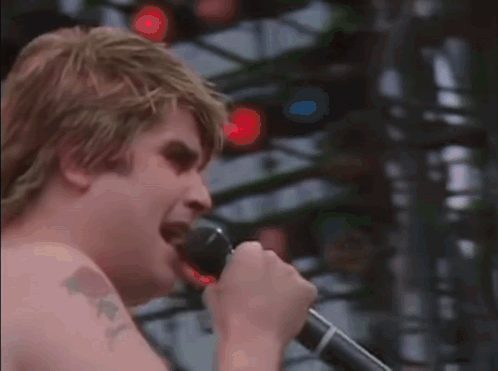 A Man With A Tattoo On His Arm Is Singing Into A Microphone .. GIF