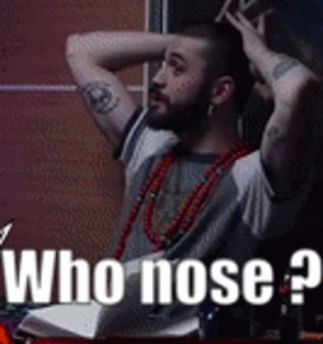 A Man With A Tattoo On His Arm Is Sitting At A Table With His Hands On His Head And The Words " Who Nose " On The Bottom GIF