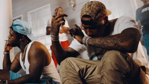 A Man With A Tattoo On His Arm Is Sitting Next To Another Man GIF