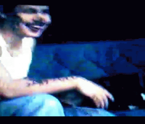 A Man With A Tattoo On His Arm Is Sitting On A Blue Couch And Smiling GIF