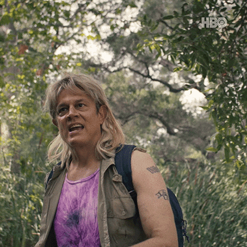 A Man With A Tattoo On His Arm Is Standing In The Woods With A Hbo Logo Behind Him GIF