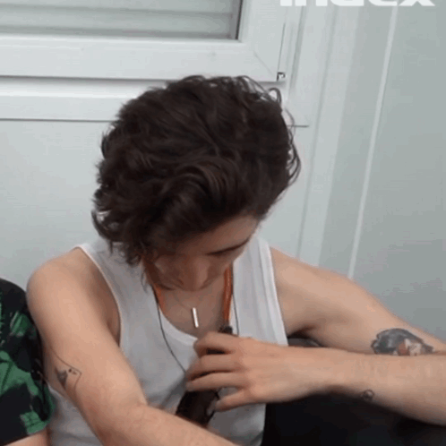 A Man With A Tattoo On His Arm Is Wearing A White Tank Top And A Necklace GIF
