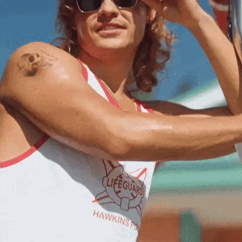 A Man With A Tattoo On His Arm Is Wearing Sunglasses And A Lifeguard Shirt . GIF