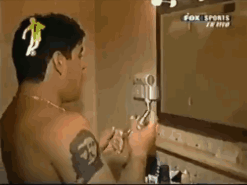 A Man With A Tattoo On His Arm Looks At Himself In A Mirror While Fox Sports Is Playing GIF