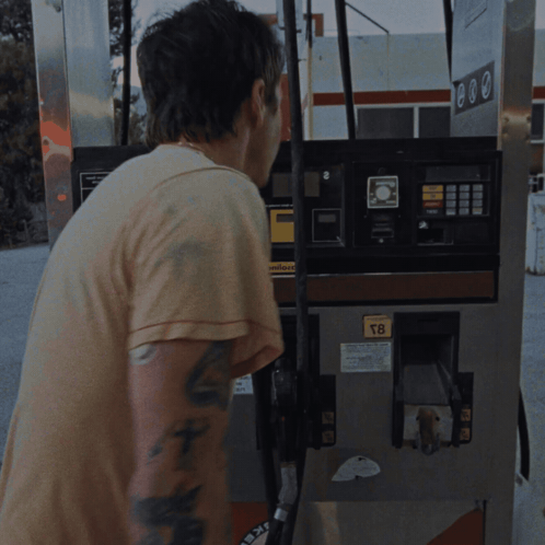 a man with a tattoo on his arm stands in front of a gas pump that says t8 on it