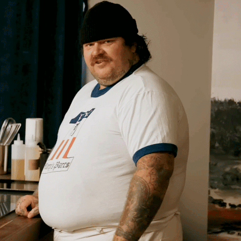 A Man With A Tattoo On His Arm Wears A Shirt That Says ' Ii ' On The Front GIF