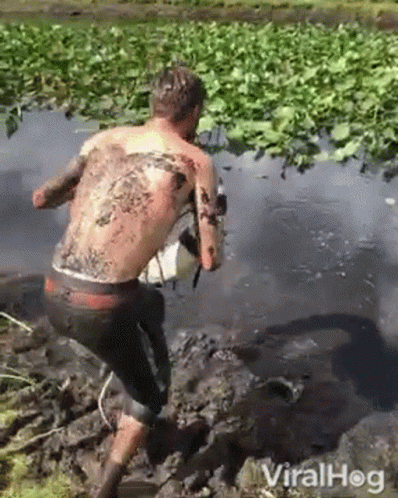 a man with a tattoo on his back is walking through the mud .