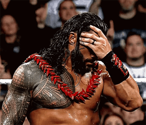 A Man With A Tattoo On His Chest Is Holding His Hand To His Head While Wearing A Lei . GIF