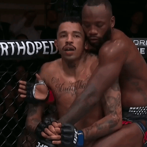 A Man With A Tattoo On His Chest Is Hugging Another Man With Ufc Gloves GIF