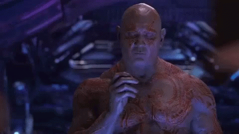 A Man With A Tattoo On His Chest Is Sitting In A Dark Room . GIF