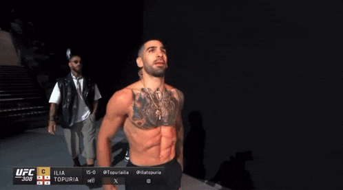 A Man With A Tattoo On His Chest Is Standing In Front Of A Ufc Advertisement GIF