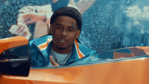 A Man With A Tattoo On His Face Is Driving An Orange Car GIF