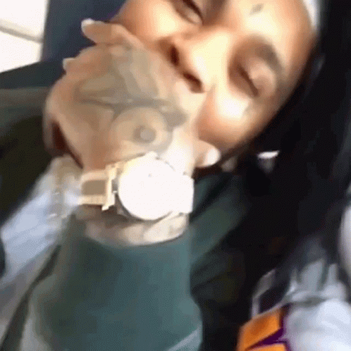 A Man With A Tattoo On His Face Is Holding A Watch In His Mouth . GIF
