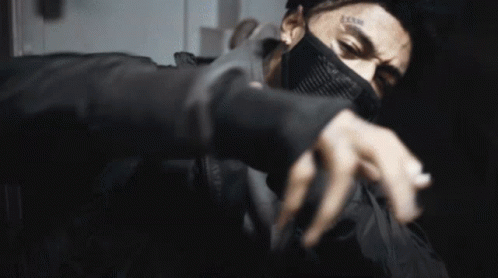 A Man With A Tattoo On His Face Is Wearing A Mask And A Ring On His Finger . GIF