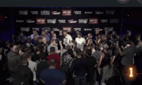 A Man With A Tattoo On His Face Stands In A Crowd With A Security Guard Behind Him GIF