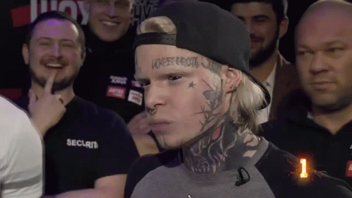 A Man With A Tattoo On His Face Stands In Front Of A Crowd Of People Wearing Security Shirts GIF
