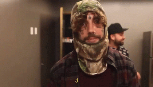 A Man With A Tattoo On His Face Wears A Camo Hood GIF