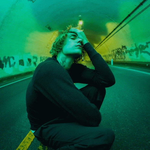 A Man With A Tattoo On His Neck Is Kneeling Down In Front Of A Green Tunnel GIF