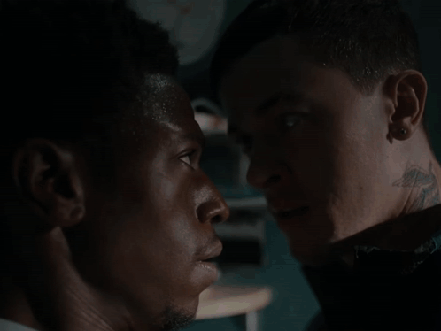 A Man With A Tattoo On His Neck Is Looking At Another Man GIF