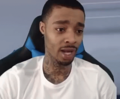 A Man With A Tattoo On His Neck Is Sitting In A Chair And Looking At The Camera . GIF