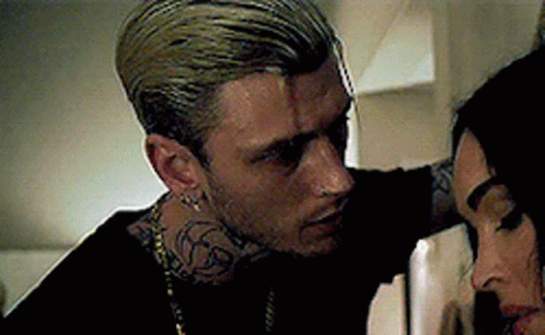 A Man With A Tattoo On His Neck Is Standing Next To A Woman . GIF