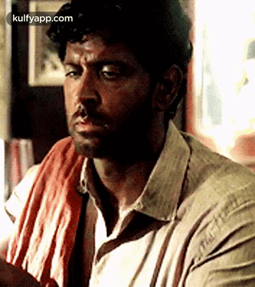A Man With A Towel Around His Neck Is Sitting In A Room . GIF