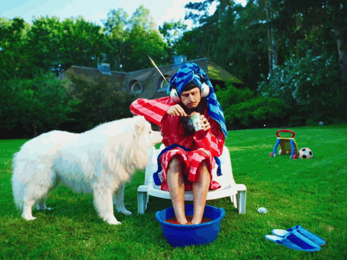 A Man With A Towel Wrapped Around His Head Sits In A Chair With A Dog GIF