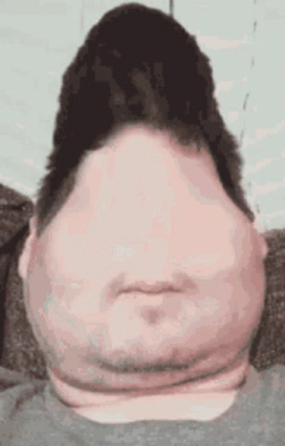 A Man With A Very Large Head And Neck Is Sitting On A Couch And Making A Funny Face . GIF
