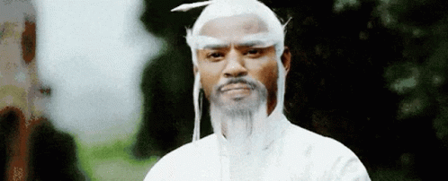 A Man With A White Wig And Beard Is Standing In Front Of Trees . GIF