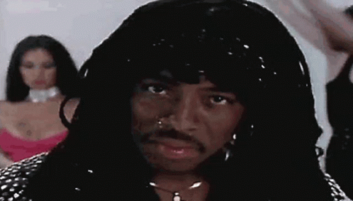 A Man With A Wig And A Mustache Is Standing In Front Of A Woman In A Pink Dress . GIF