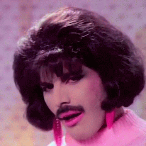 A Man With A Wig And Mustache Is Wearing A Pink Sweater And Pink Earrings . GIF