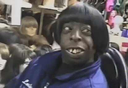 A Man With A Wig On His Head Is Sitting In A Chair In Front Of A Mannequin . GIF
