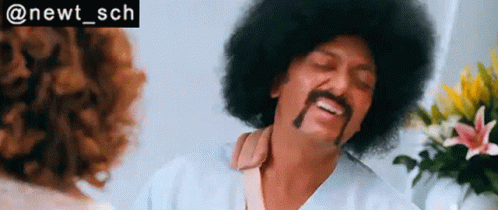 A Man With An Afro And Mustache Is Talking To A Woman In A Room . GIF