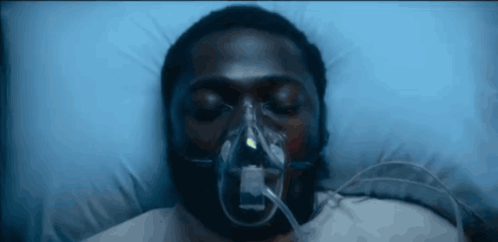 A Man With An Oxygen Mask On His Face Is Laying In A Hospital Bed GIF
