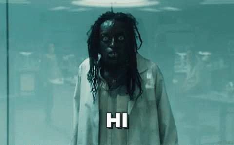 A Man With Black Hair And Dreadlocks Is Wearing A Lab Coat And A Mask And Saying Hi . GIF