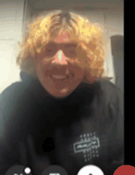 A Man With Blonde Curly Hair Is Smiling While Wearing A Black Shirt With The Letter R On It GIF