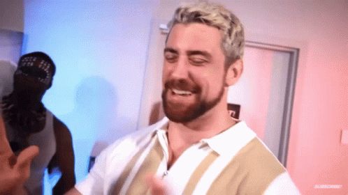 A Man With Blonde Hair And A Beard Is Smiling In Front Of A Door GIF