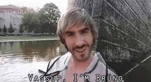 A Man With Blonde Hair And A Beard Is Standing Next To A Body Of Water And Smiling . GIF