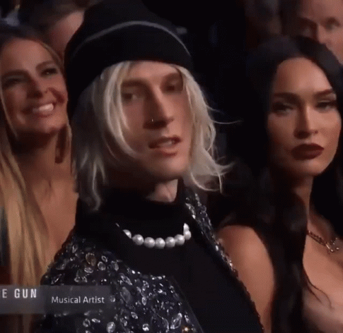 A Man With Blonde Hair And A Pearl Necklace Is Standing In A Crowd Of People With The Word Musical Artist On The Bottom GIF