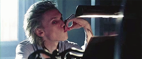 A Man With Blonde Hair Is Licking His Nose While Looking At A Mirror . GIF