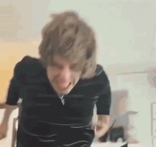 a man with blonde hair is making a funny face while standing in front of a table .